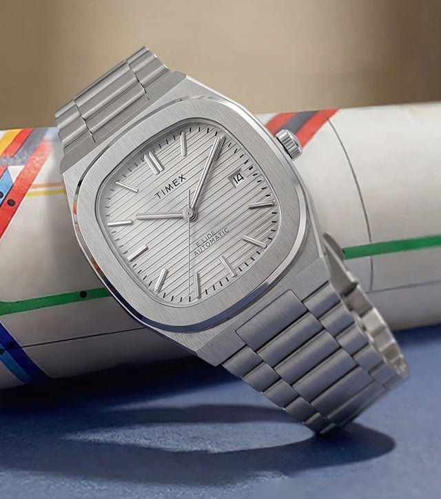 Timex Automatic E Line 38mm with a silver-tone dial and stainless-steel bracelet, displayed against a colorful transit map.
