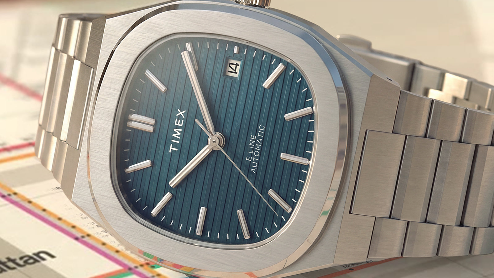 Close-up of the Timex® Automatic E Line 38mm featuring a blue vertically textured dial, date window, brushed stainless steel case, and integrated stainless steel bracelet.