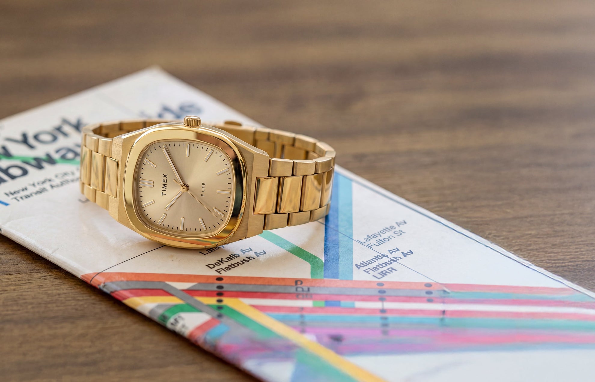 Timex® Quartz E Line 30mm watch with a gold-tone stainless steel bracelet and champagne dial displayed on a New York City subway map.