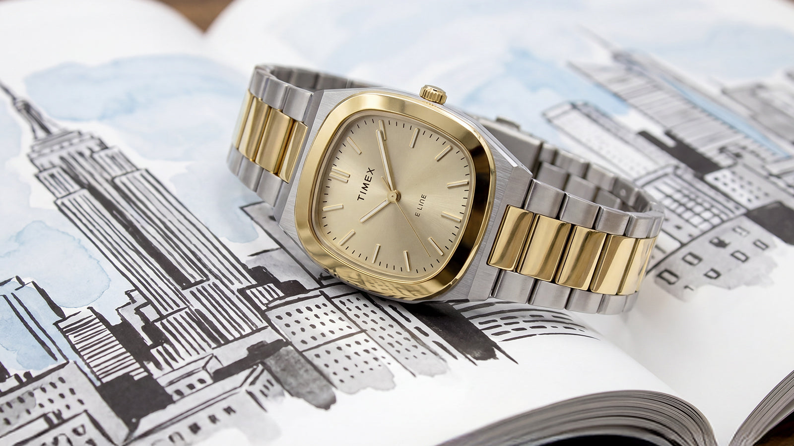 Close-up of the Timex® Quartz E Line 30mm with a two-tone stainless steel bracelet and champagne dial resting on an illustrated cityscape book.
