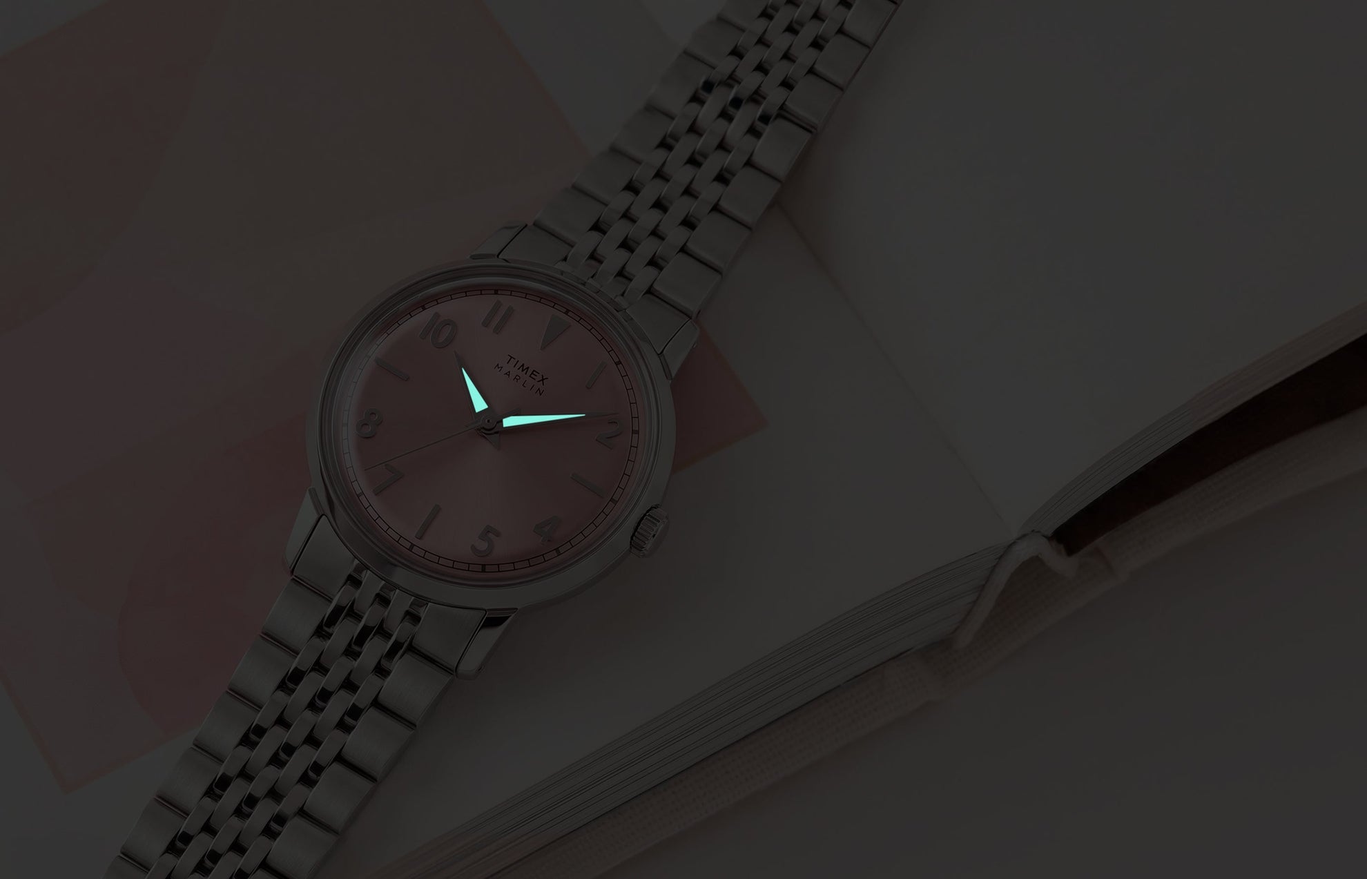 Timex Marlin Quartz watch with luminous hands glowing in low light against a pink sunray dial.