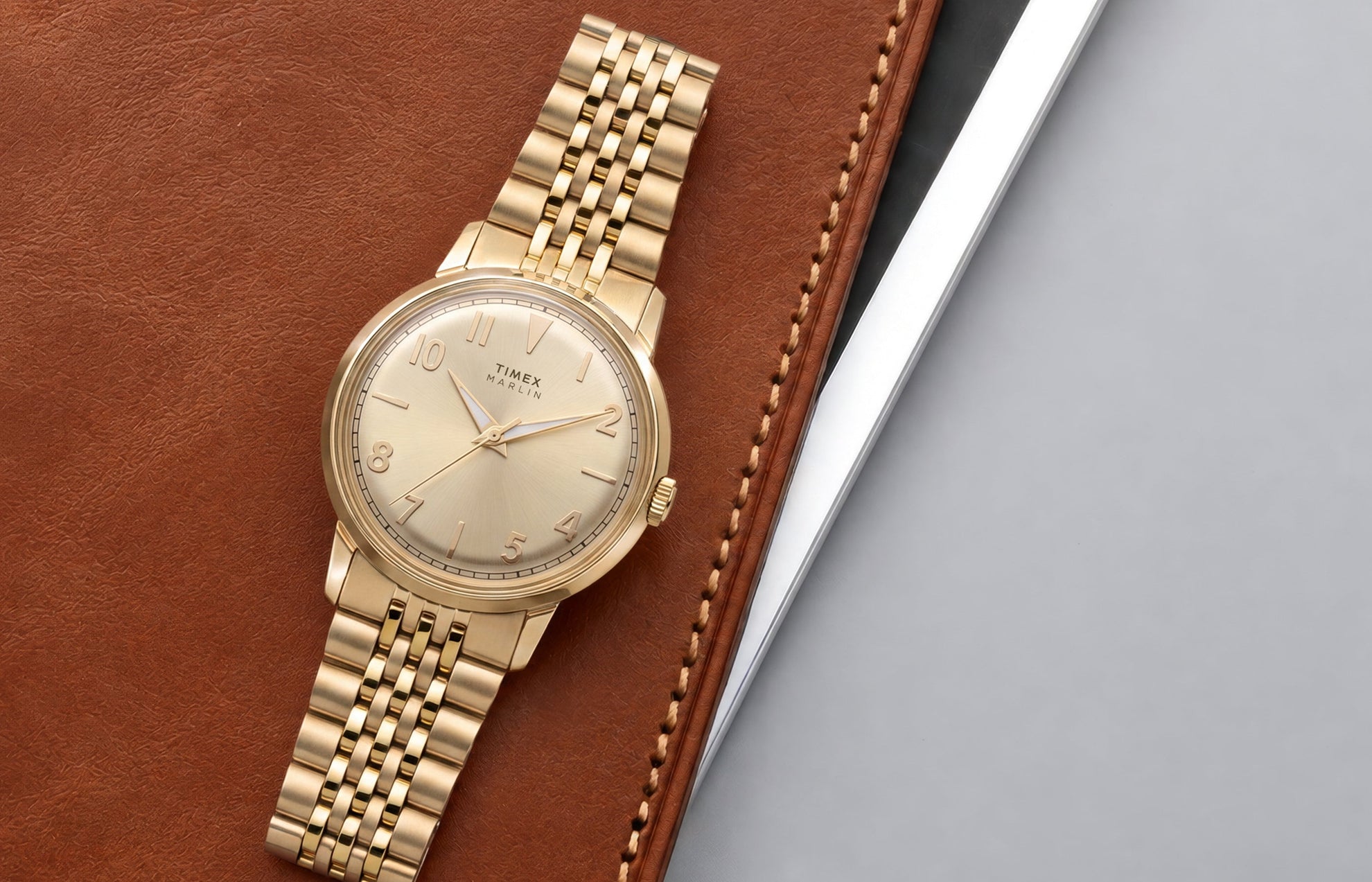 Timex Marlin Quartz watch with a champagne sunray dial and gold-tone stainless steel bracelet displayed on a leather portfolio.