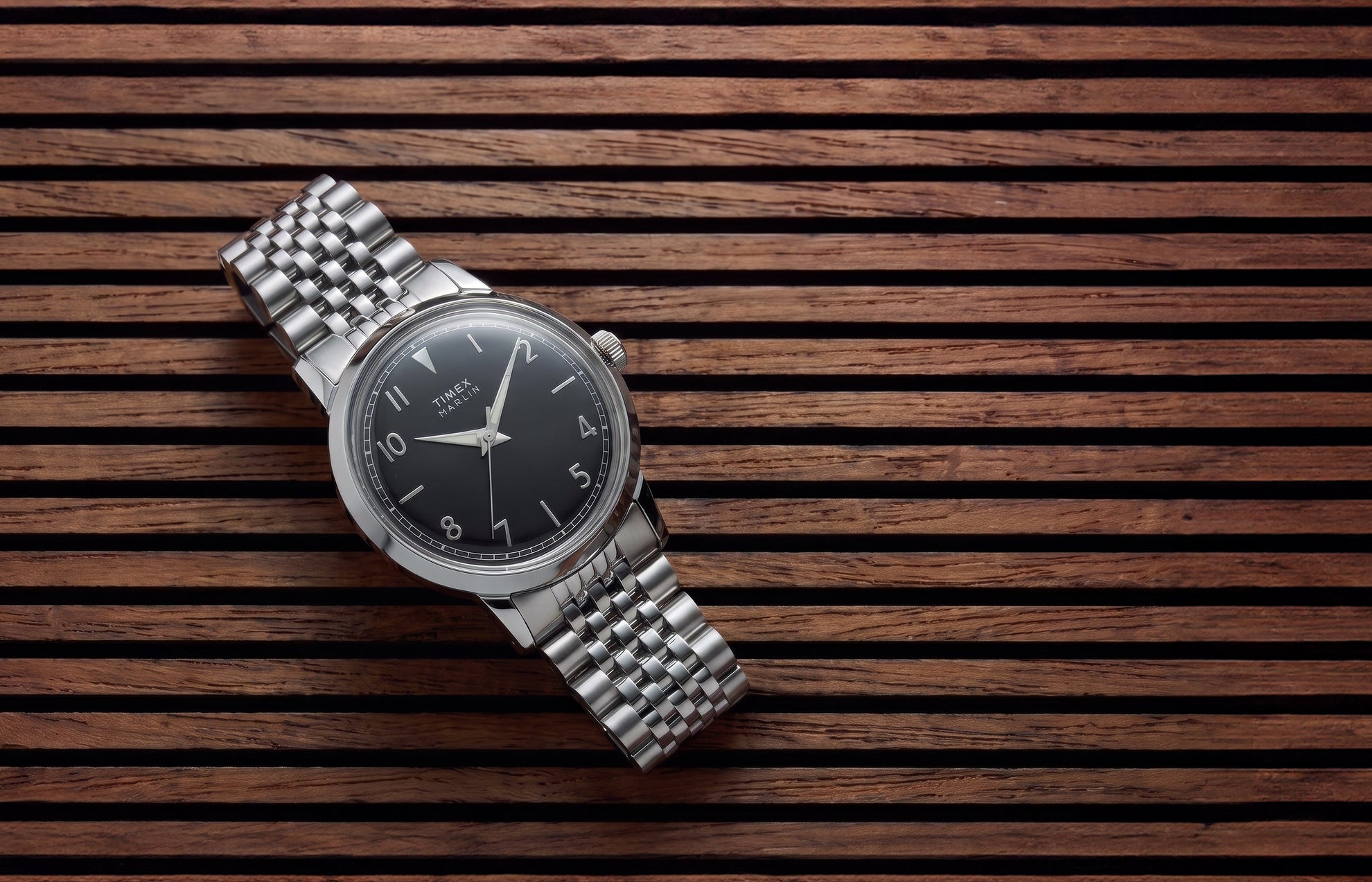 Timex Marlin Quartz watch with a black sunray dial and stainless steel bracelet displayed on a slatted wood surface.