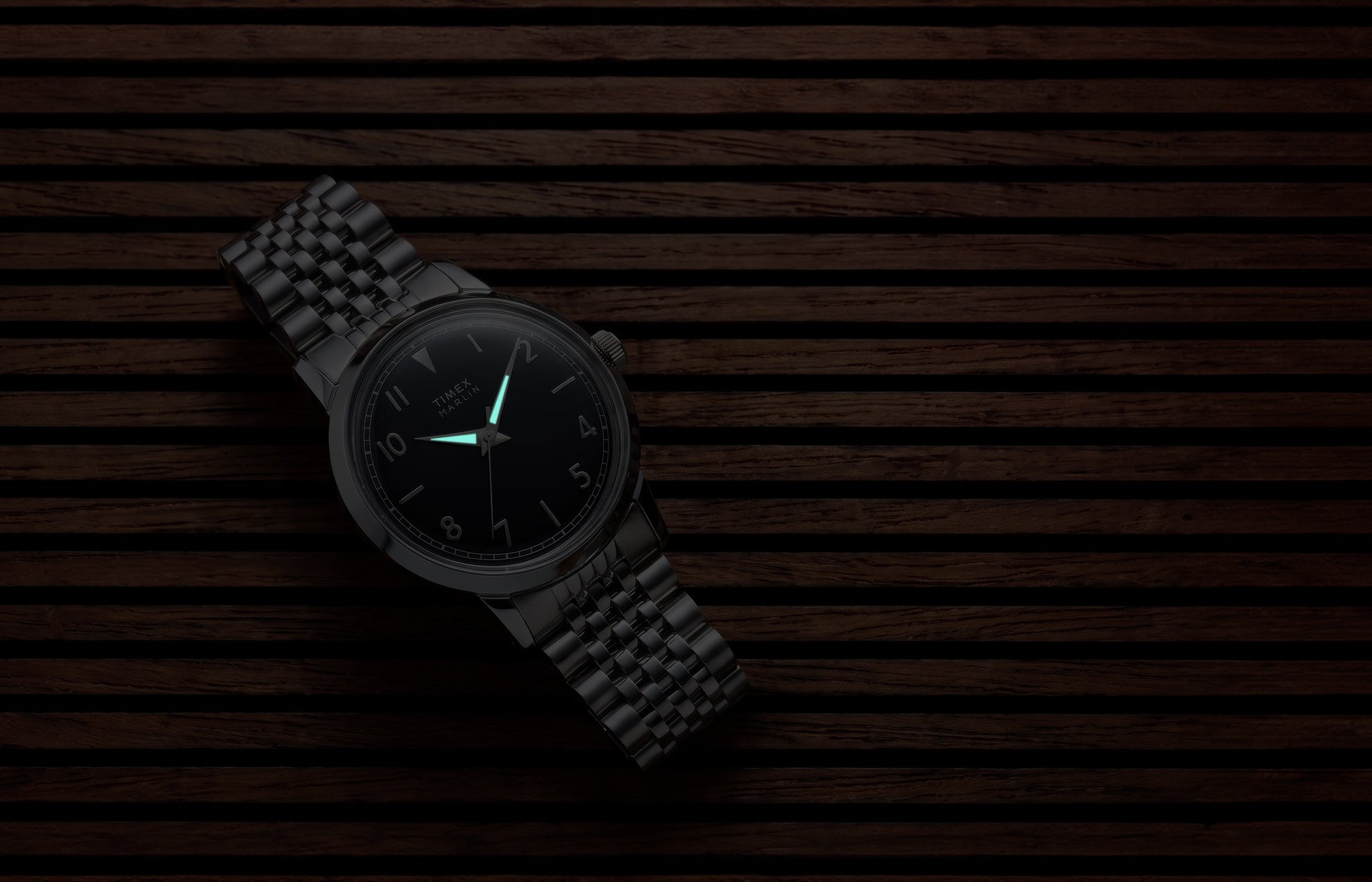 Close-up of the Timex Marlin Quartz with luminous hands illuminated on a black sunray dial in low light.