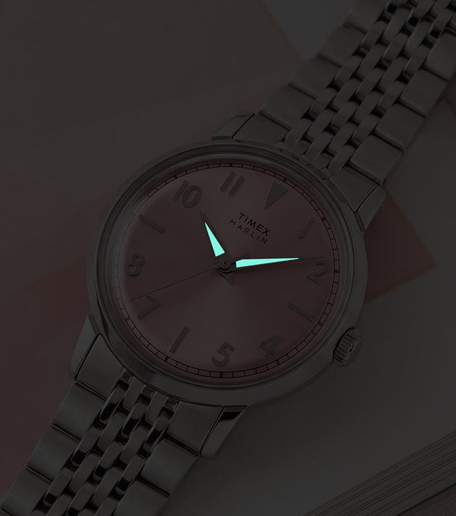 Timex Marlin Quartz watch with luminous hands glowing in low light against a pink sunray dial.