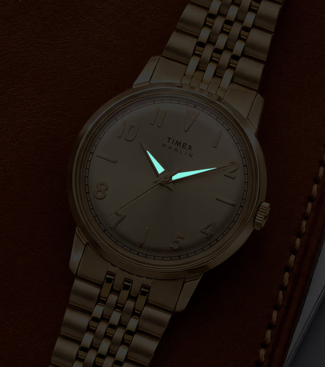 Timex Marlin Quartz watch with luminous hands glowing in low light against a champagne sunray dial.