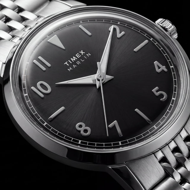 Macro view of the Timex Marlin Quartz black sunray dial with applied silver-tone Arabic numerals, luminous hands, and polished stainless steel case.