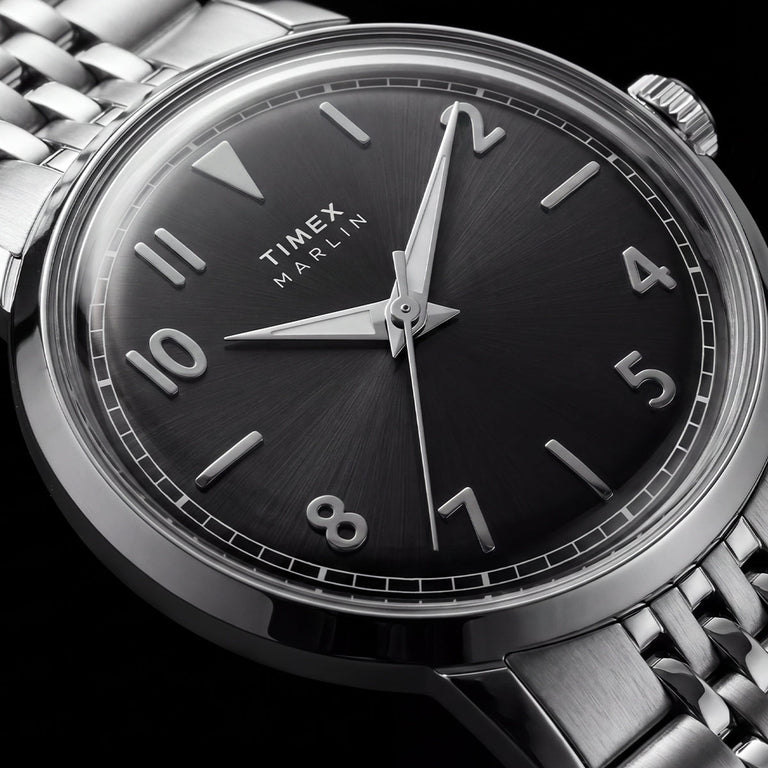 Macro view of the Timex Marlin Quartz black sunray dial with applied silver-tone Arabic numerals, luminous hands, and polished stainless steel case.