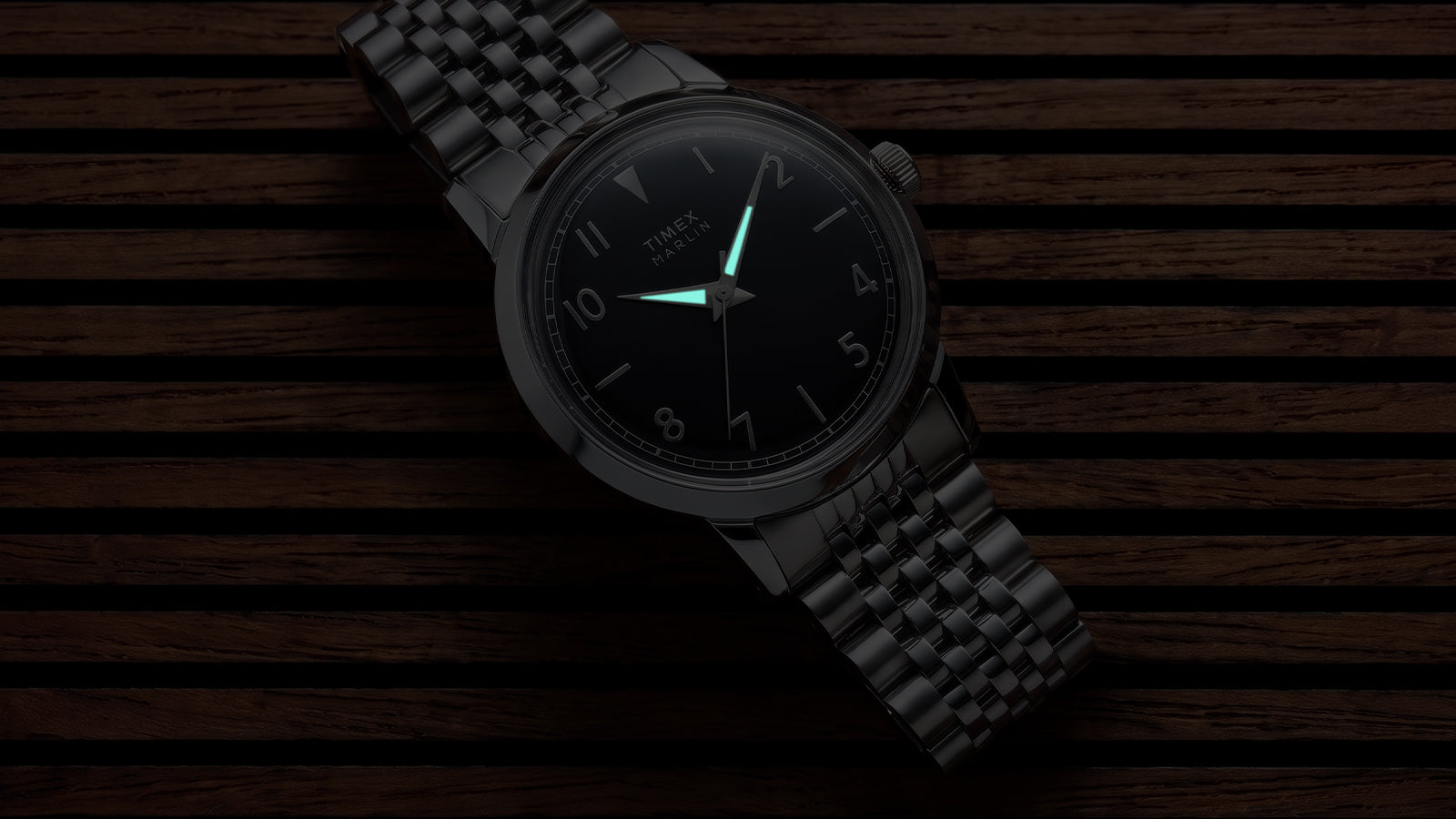 Timex Marlin Quartz with luminous hands glowing in low light against a black sunray dial.