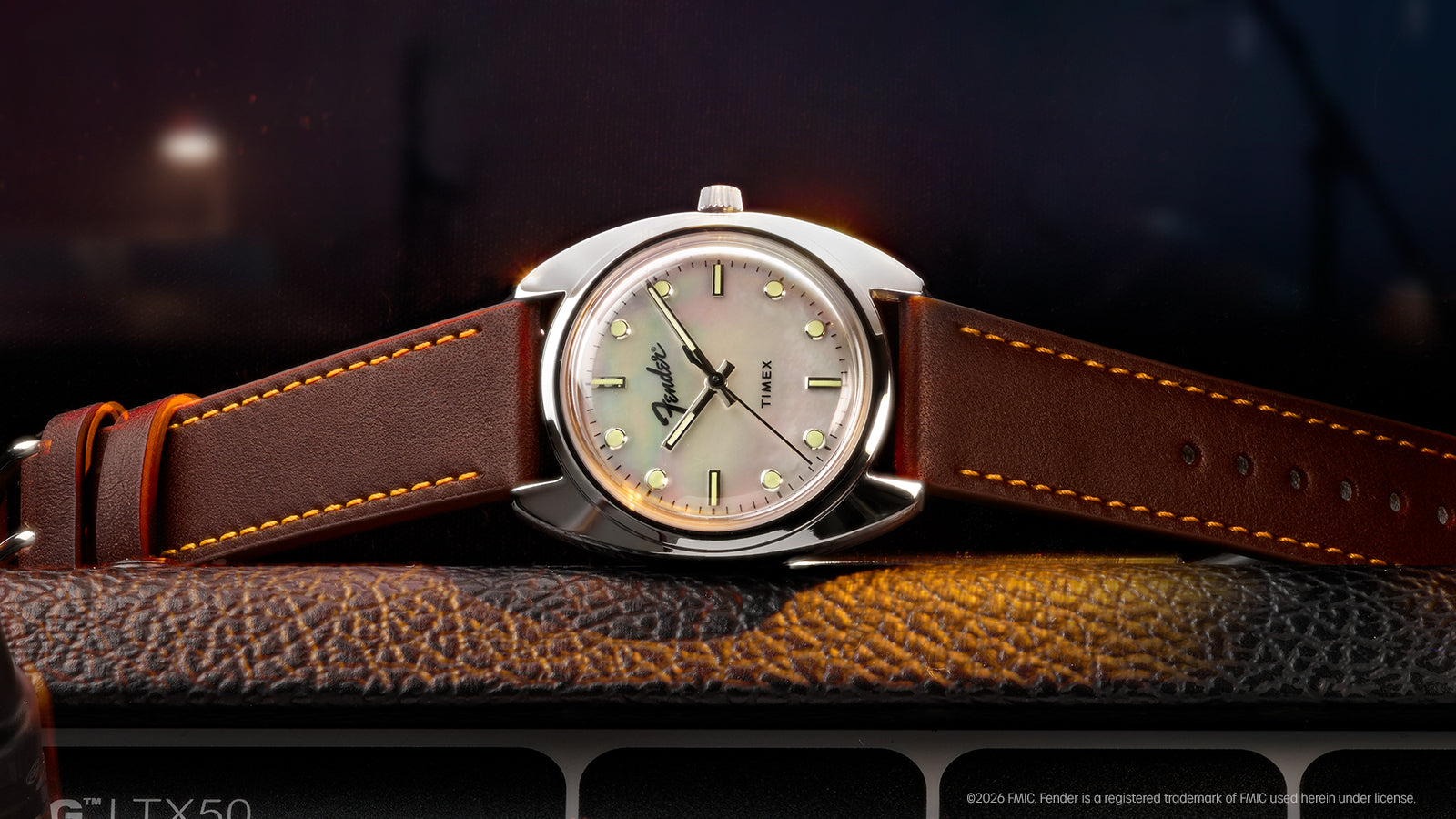 Fender x Timex watch with a mother-of-pearl dial and brown leather strap displayed across a guitar amplifier.