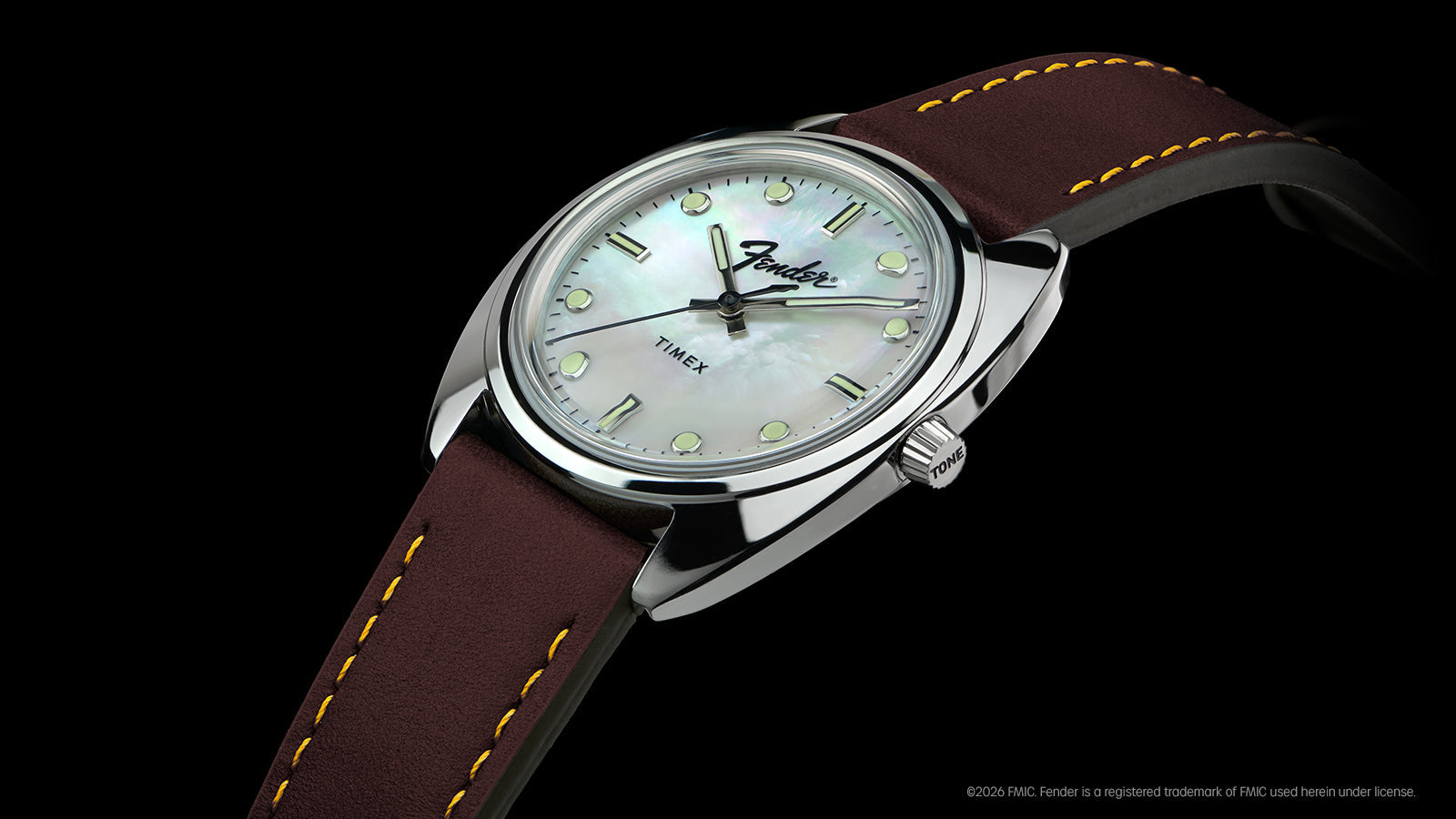 Fender x Timex watch shown at an angle against a black background, featuring a silver-tone case and brown leather strap.