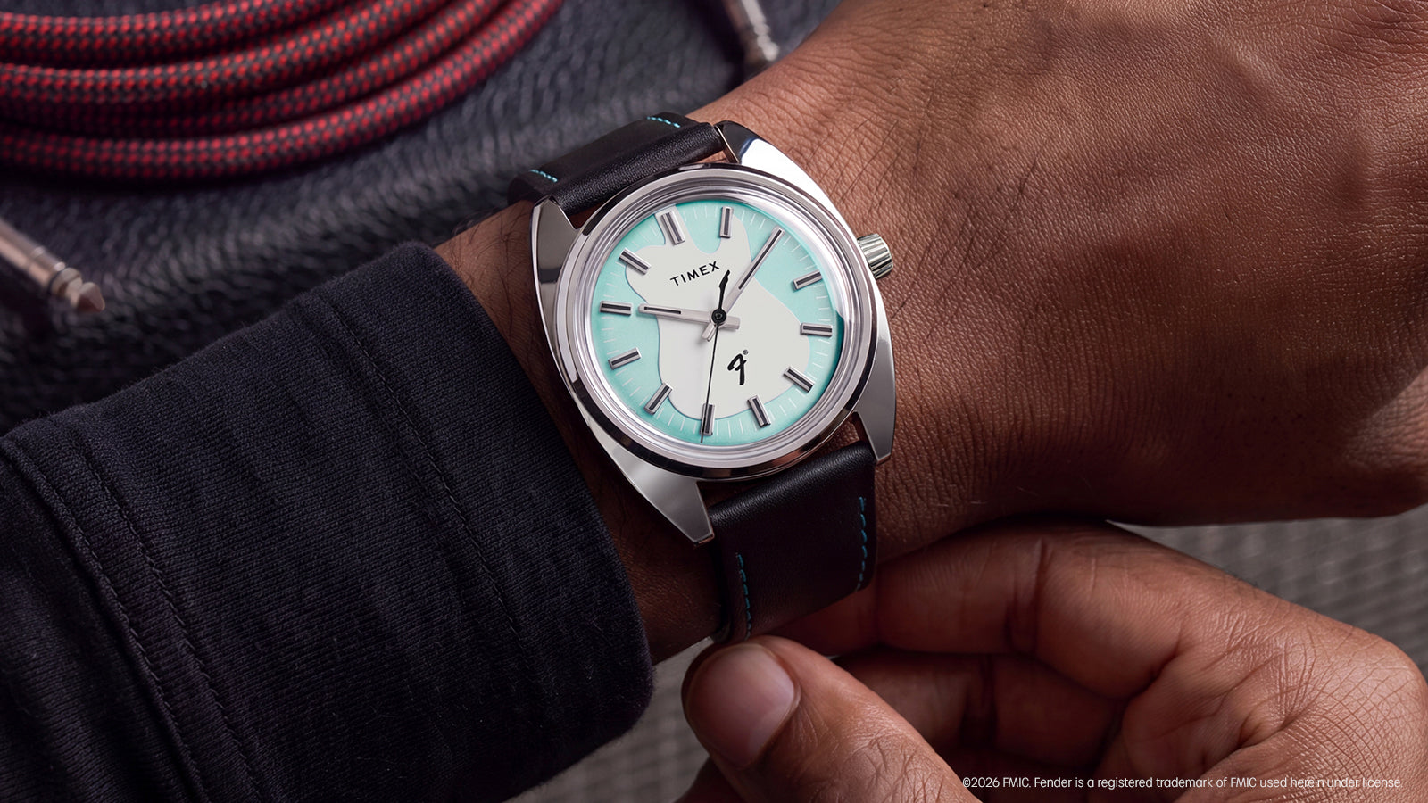 Close-up of the Fender x Timex watch worn on the wrist beside a coiled guitar cable.