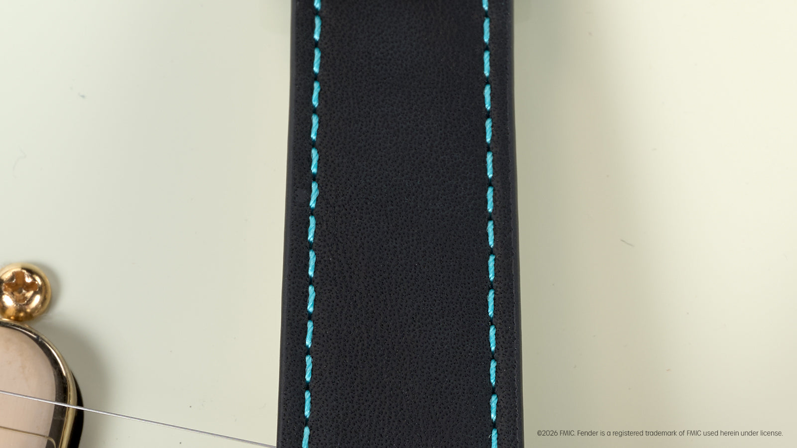 Close-up of the black watch strap with turquoise stitching displayed across a Fender electric guitar.