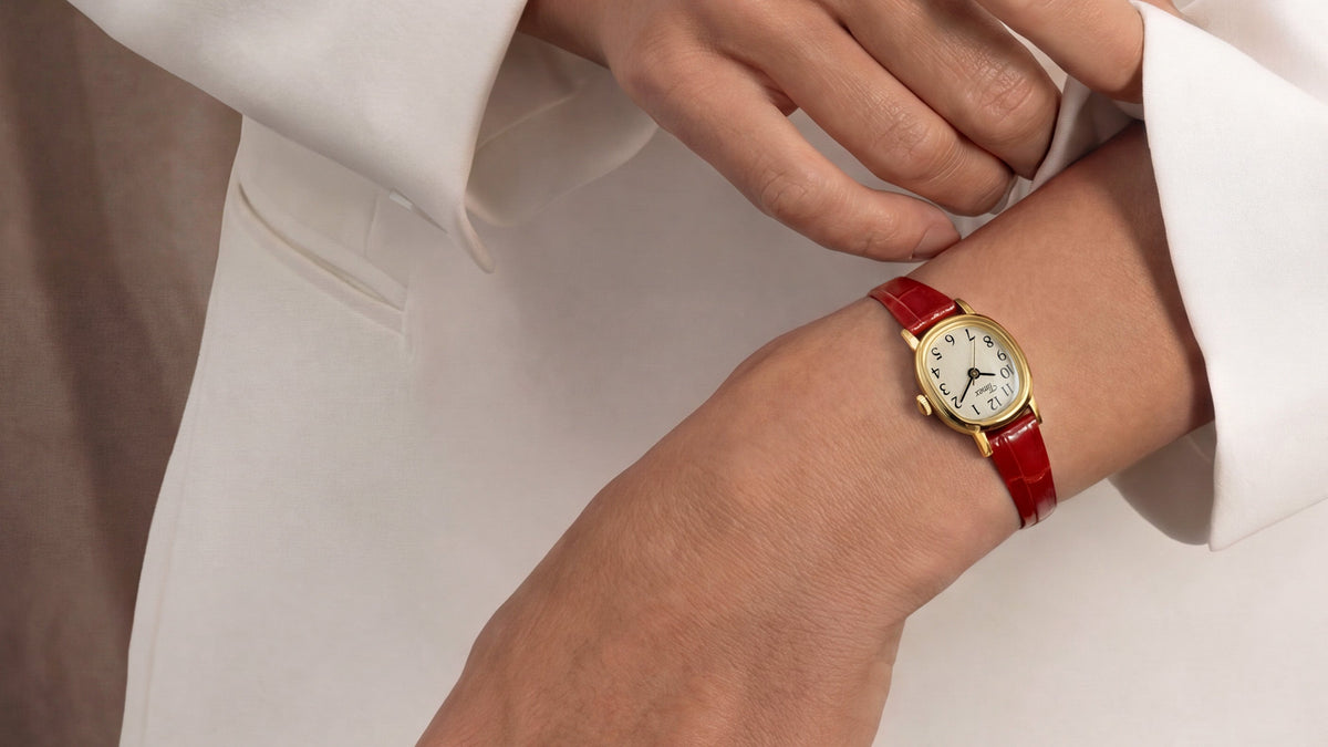 Cavatina® Mini watch with a gold-tone case and red leather strap worn on a wrist with a white outfit.