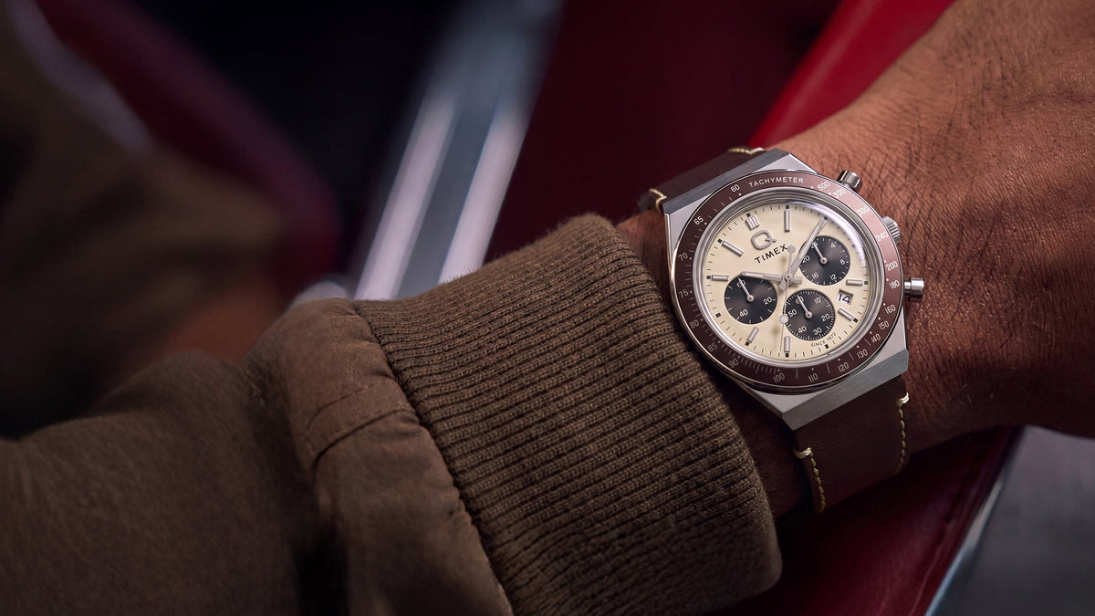 Q Timex Chronograph with a cream dial and brown leather strap styled on the wrist inside a red car interior.