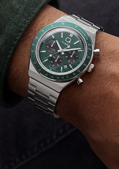 Q Timex Chronograph with a green dial and stainless-steel bracelet styled with a dark green jacket.