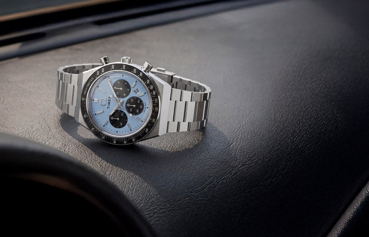 Q Timex Chronograph with an ice-blue dial and stainless-steel bracelet displayed on a black leather surface.