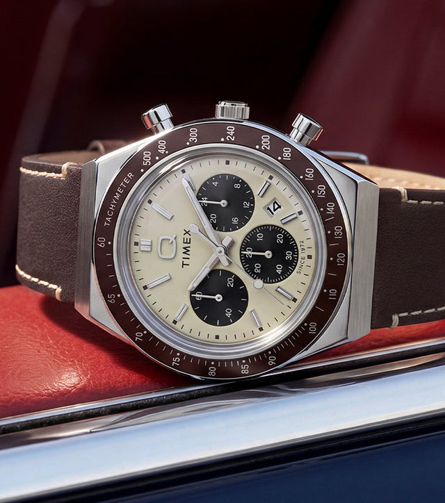 Q Timex Chronograph with a cream dial and brown leather strap displayed inside a red car interior.