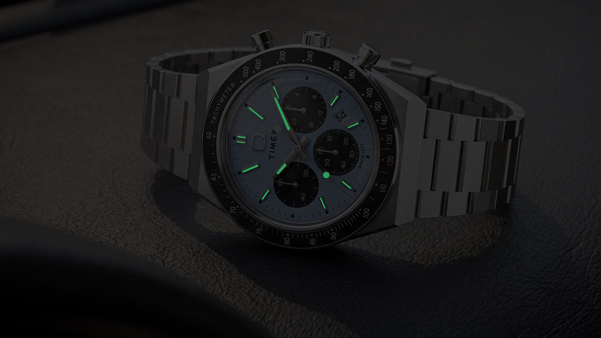 Q Timex Chronograph in darkness with illuminated hands and hour markers.