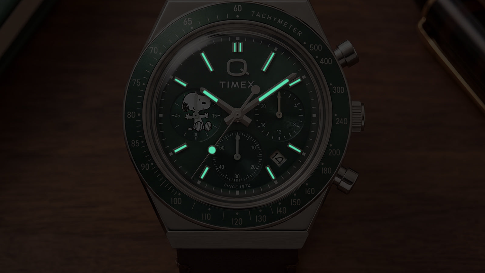 Close-up of the Peanuts® x Q Timex Chronograph dial in low light, highlighting its luminous hands and hour markers.