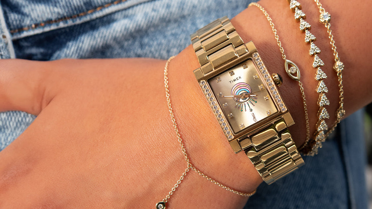 Gold-tone Timex x Jacquie Aiche Éclat watch worn with layered gold and crystal bracelets.