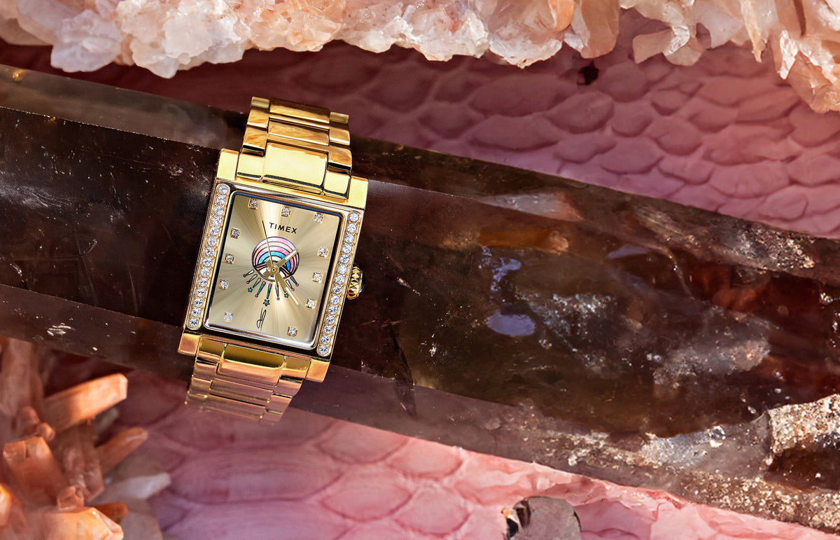 Gold-tone Timex x Jacquie Aiche Éclat watch with a champagne dial, crystal accents, and colorful eye motif among pink crystals.
