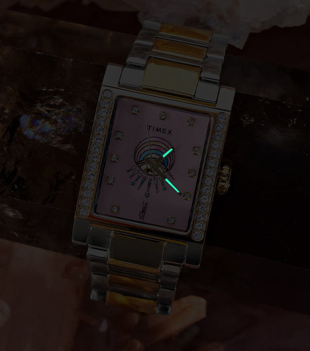 Timex x Jacquie Aiche Éclat watch in low light, revealing glowing hands against its pink dial.