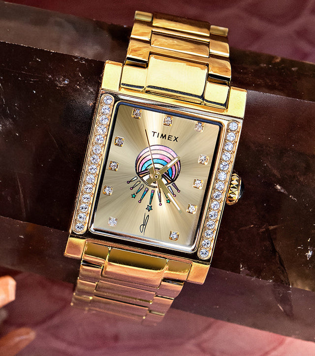 Gold-tone Timex x Jacquie Aiche Éclat watch with a champagne dial, crystal accents, and colorful eye motif among pink crystals.