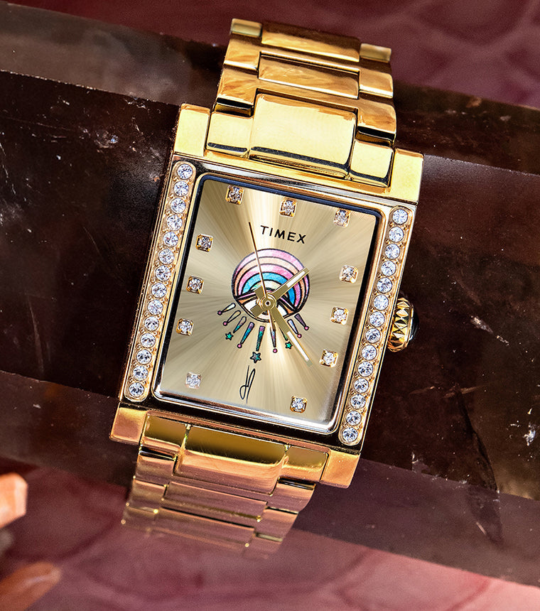 Gold-tone Timex x Jacquie Aiche Éclat watch with a champagne dial, crystal accents, and colorful eye motif among pink crystals.
