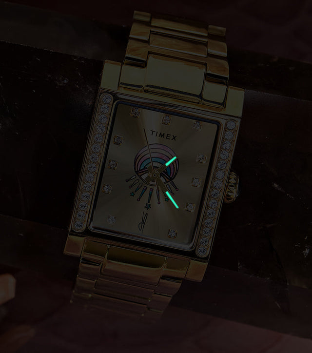 Gold-tone Timex x Jacquie Aiche Éclat watch in low light, showing glowing hands against its champagne dial.