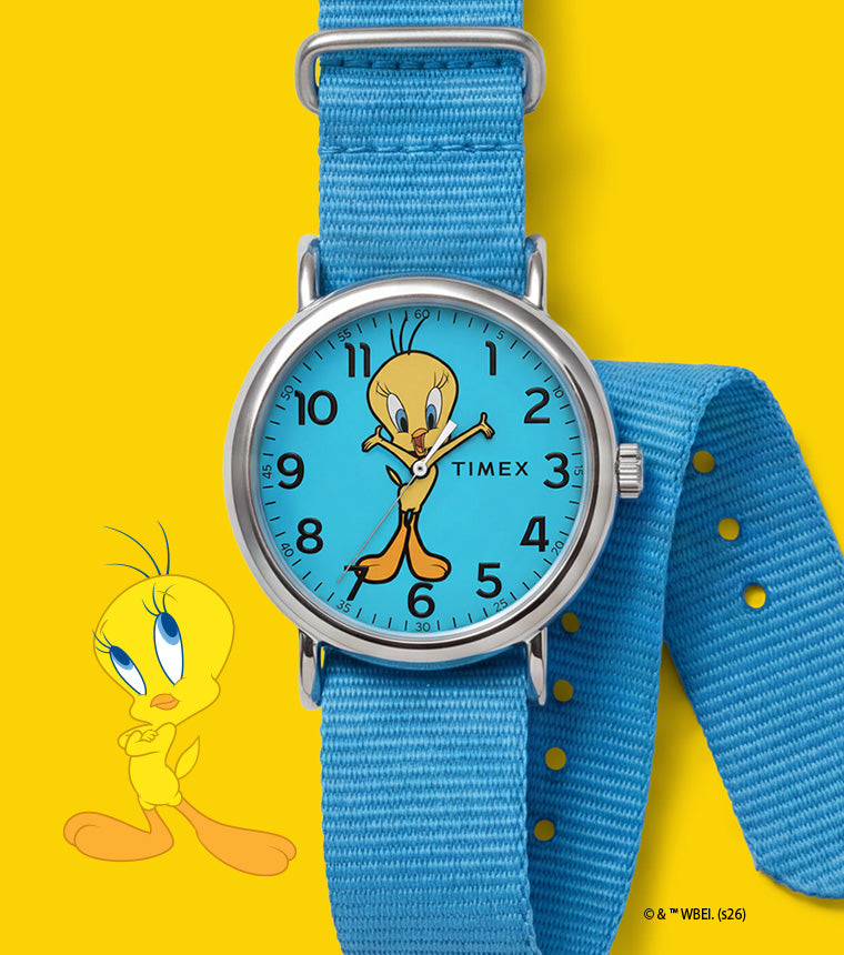 TW2Y99500 Looney Tunes Tweety Bird x Timex Weekender watch with a blue character dial and blue fabric strap beside Tweety artwork on yellow.