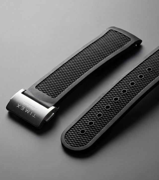 Timex Atelier NBR synthetic rubber strap in black with a textured finish and stainless-steel clasp, displayed against a dark background.