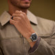 Person wearing the MK1® Automatic watch with a tan fabric strap and an olive-green jacket.