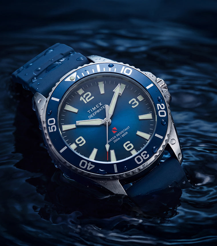 TW3A01900 Deepwater Arctic 200 watch with a blue dial and strap resting in dark, rippling water.