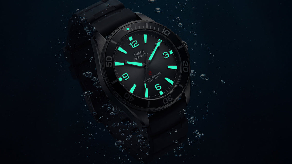 TW3A02000 Angled view of the Deepwater Arctic 200 watch with glowing aqua hands and hour markers amid underwater bubbles.