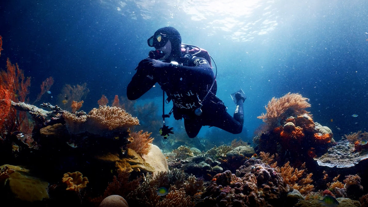 TW3A02000 Scuba diver swimming above a colorful coral reef in clear blue water.