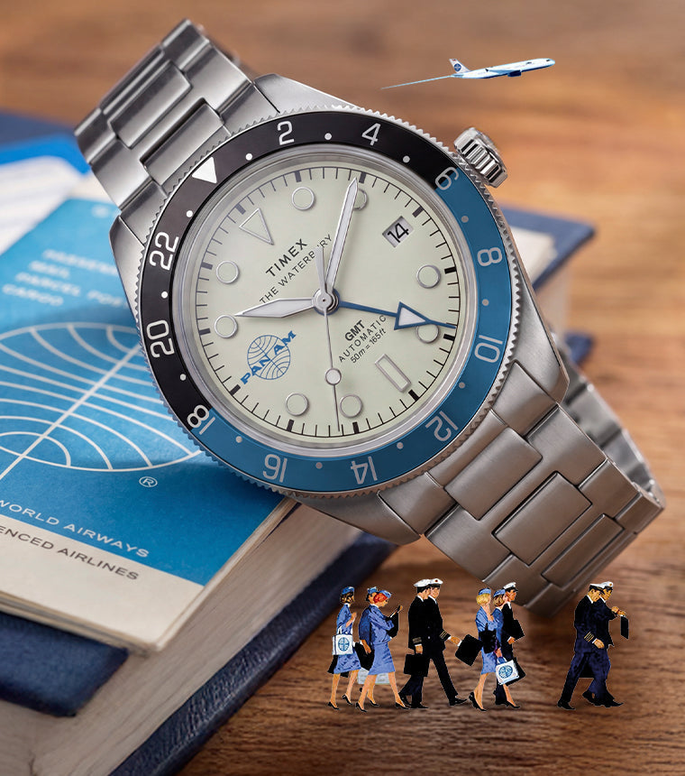 TW2Y94300 Pan Am x Timex Waterbury Automatic GMT watch beside a Pan Am travel book with miniature airline crew and airplane details.