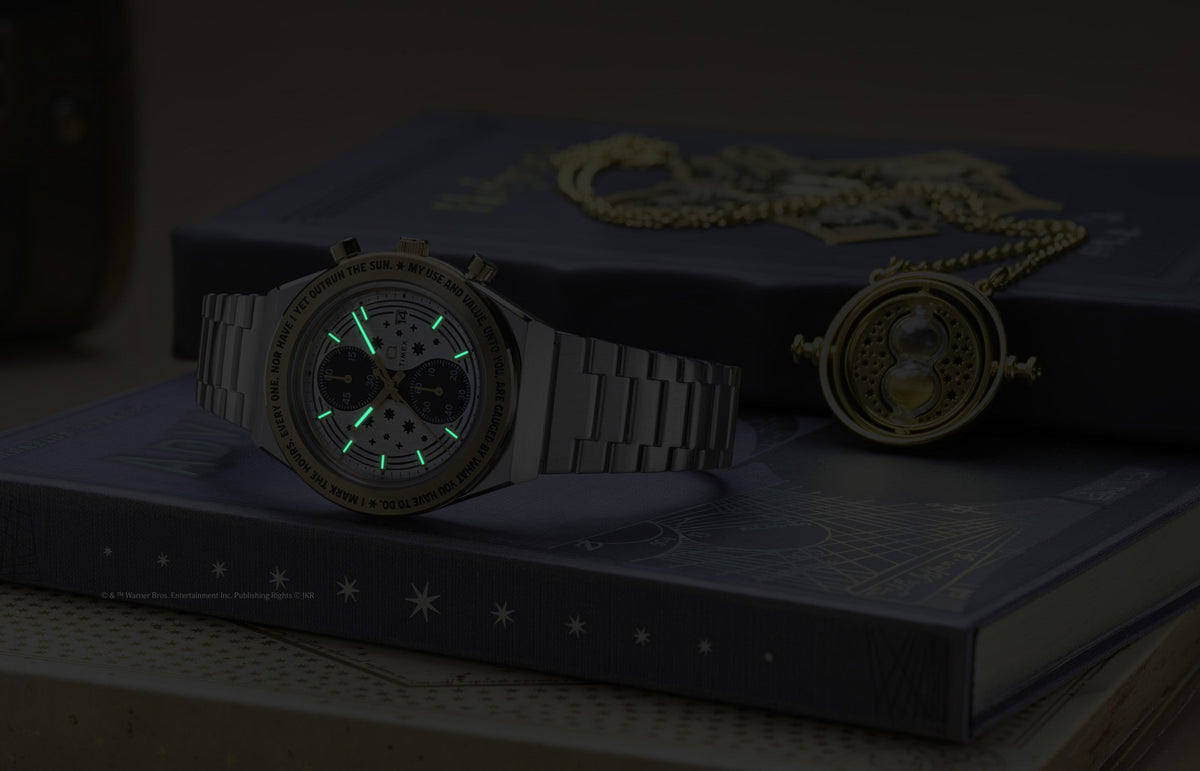 TW2Y75900 The watch and Time-Turner pendant in dim light, showing the watch’s glowing hands and hour markers.