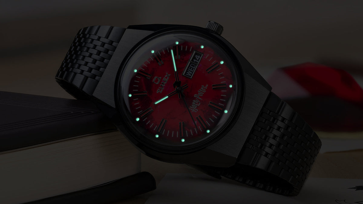 TW2Y99700 Harry Potter x Q Timex watch shown in darkness with luminous green hands and hour markers glowing against the red dial.