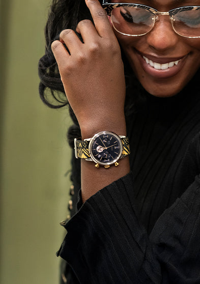 TWG069100 Smiling woman wearing glasses and the black-dial watch with a black-and-gold patterned strap.