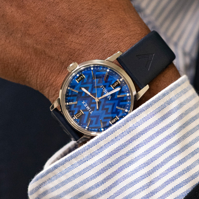 TW2Y73800 Close-up of the blue-dial watch worn with a striped shirt and dark jacket.