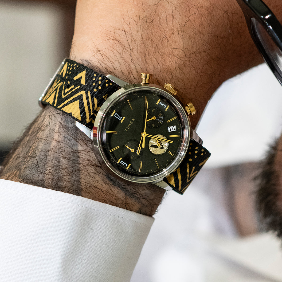 TWG069100 Close-up of the black-dial watch with a black-and-gold patterned strap worn on a wrist.