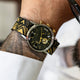 TWG069100 Close-up of the black-dial watch with a black-and-gold patterned strap worn on a wrist.