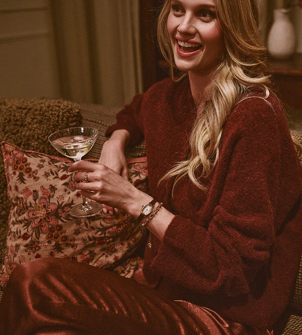 Gifts for Her - Smiling woman in a red sweater wearing a gold-tone Timex watch and holding a stemmed glass.
