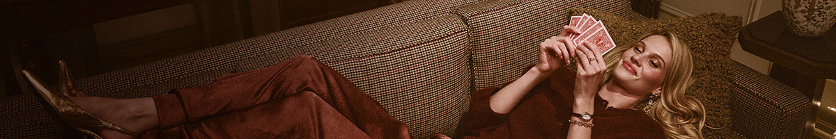 Gifts for Her - Woman reclining on a patterned sofa, holding playing cards and wearing a gold-tone Timex watch.