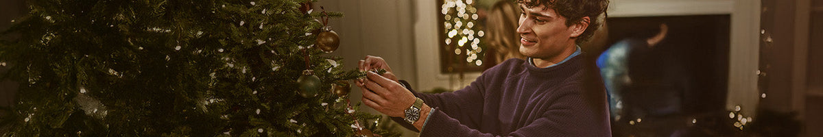 Gifts for Him - Man wearing a Timex watch with a green strap while decorating a Christmas tree.