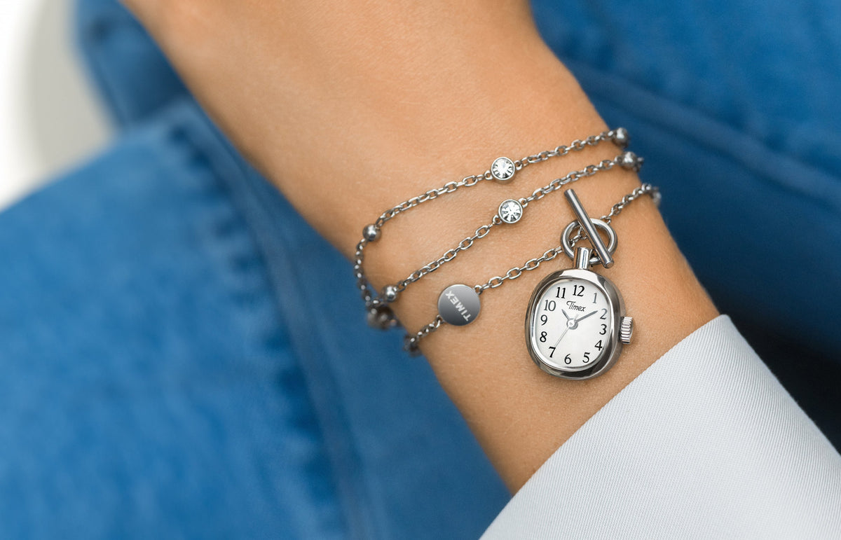 TW6A17600 Close-up of the Cavatina® Mini watch necklace worn around a wrist beside a white cuff, against blue denim.