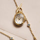 TW6A17700 Cavatina® Mini gold-tone watch pendant with black Arabic numerals, beside a chain with clear stones on cream paper.