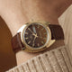 TW2Y87200 Wrist close-up of the Timex 1978 Day Date Fumé Reissue with a gold-tone case, brown leather strap, and day-date display.