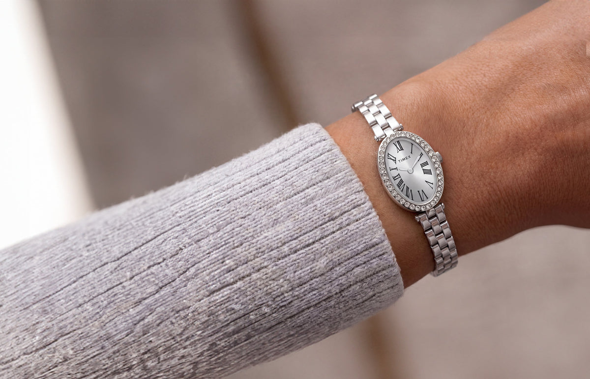 TW2Y90000 Timex Cavatina® Crystals watch with a silver-tone link bracelet and oval Roman numeral dial, worn beside a light gray knit sleeve.
